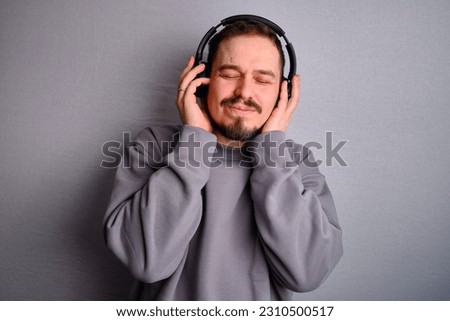 Happy handsome man in headphones and casual wear sweatshirt listens to a sound show. Good posing isolated on a light studio background. Music concept and emotions