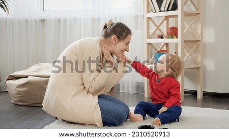 Happy smiling mother playing with her cute baby son on carpet in living room.
