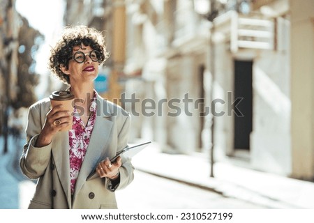 Shot of a confident young businesswomen out and about in the city. Beautiful young business woman smiling and holding documents and coffee to go. A coffee break gives a boost to the day