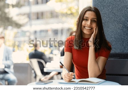 Smiling smart student studying, learning language, exam preparation sitting in university campus, education concept. Portrait of successful asian businesswoman, young writer taking notes in cafe  Royalty-Free Stock Photo #2310542777