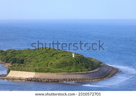 Concrete sea wall protects coastline on small green island with lighthouse Royalty-Free Stock Photo #2310572701