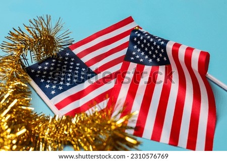 Small America national flags with golden tinsel garland isolated on blue background. Celebration and USA Independence Day concept.  Royalty-Free Stock Photo #2310576769