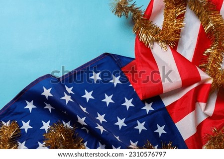 Beautifully waving star and striped American flag with golden tinsel garland decoration on blue background with copy space. Celebration and USA Independence Day concept Royalty-Free Stock Photo #2310576797