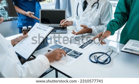 Medical surgical team meeting with doctors in white lab coats and surgical gowns sitting at table discussing x-ray of patient history. success of medical health care.