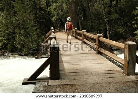 Man Walking Across Bridge over a River Royalty-Free Stock Photo #2310589997