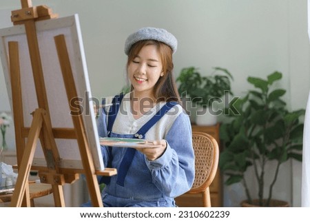 Young female artist mix color on palette to painting artwork on canvas with enjoying in home studio.