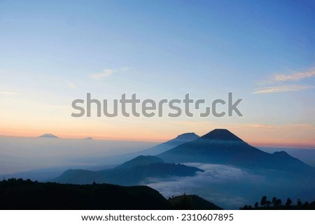 VView of three mountains from the top of Mount Prau.  The color gradation of the sky is bluish yellow and clean without clouds..