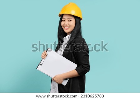 Portrait of happy smiling woman in yellow helmet and black suit She looks at the camera while standing and holding a clipboard with documents isolated over a green background.