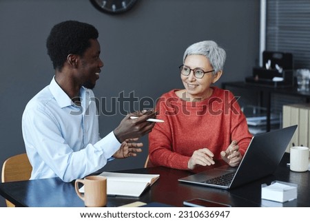 Portrait of smiling senior businesswoman working with colleague at desk in office