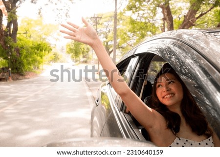 A beautiful young Asian woman hand over of the car window, a radiant smile adorning her face, exuding sheer happiness as she embarks on her holiday. Concept of driving, travel and vacation