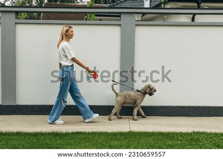 Side view of a blond woman taking the dog for a walk. Royalty-Free Stock Photo #2310659557