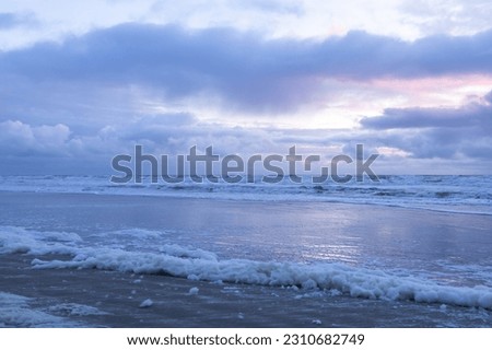 Seascape with cloudy sky, stormy sea and sandy shore and foam gathering on the shore