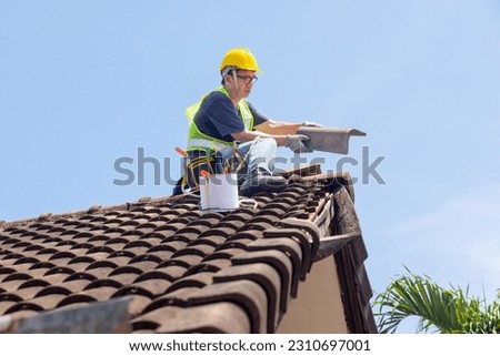 Worker man repairing eaves and tile of the old roof. Royalty-Free Stock Photo #2310697001