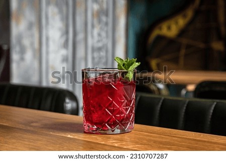 A red alcoholic cocktail in a rocks glass served on ice and garnished with mint on a wooden table in a restaurant or bar, horizontal photo Royalty-Free Stock Photo #2310707287