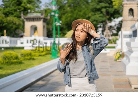 Portrait of Asian female traveler fanning and sweating on sidewalk of temple on street in Bangkok, Thailand, Southeast Asia in hot weather and temperature. Heatstroke Outdoor health problem concept Royalty-Free Stock Photo #2310725159