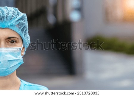 Medicine, profession and healthcare concept. Close up of face female doctor or nurse wearing a protective face mask and uniform next to a hospital on blurred background, outdoor shot. Sun glare effect