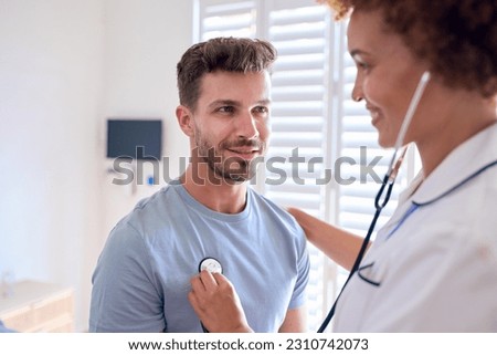 Female Nurse Wearing Uniform Listening To Male Patient's Chest In Private Hospital Room