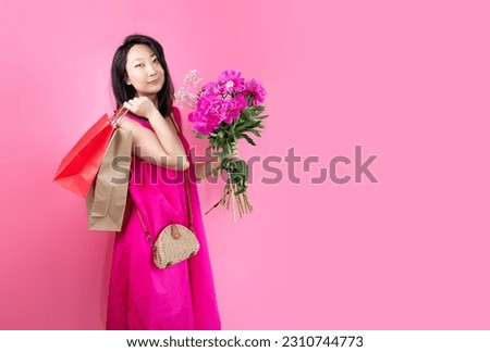 Portrait of a lovely young Asian woman in a summer dress, Female shopper in casual clothing holding two paper shopping bags and bouquet of peonies.