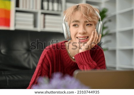 A happy and smiling young Asian gay man is daydreaming while enjoying the music in his living room. Lifestyle concept Royalty-Free Stock Photo #2310744935