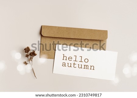 Autumn come concept Top view white paper card with word hello autumn and craft paper envelopment with trend dry flower, fall beige brown colors still life photo, minimal floral flat lay, sun glare