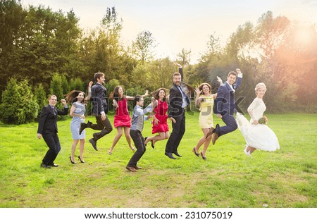 Full length portrait of newlywed couple with bridesmaids and groomsmen jumping in green sunny park
