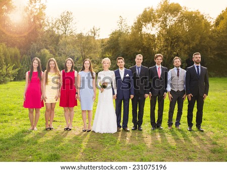 Full length portrait of newlywed couple posing with bridesmaids and groomsmen in green sunny park