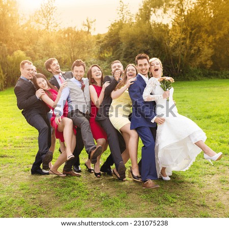 Full length portrait of newlywed couple having fun with bridesmaids and groomsmen in green sunny park