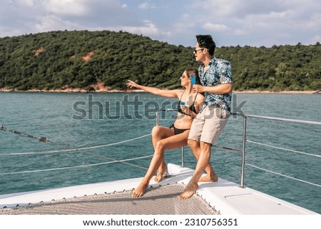 Asian beautiful couple drinking champagne while having party in yacht. Attractive man and woman hanging out, celebrating anniversary honeymoon trip while catamaran boat sailing during summer sunset.