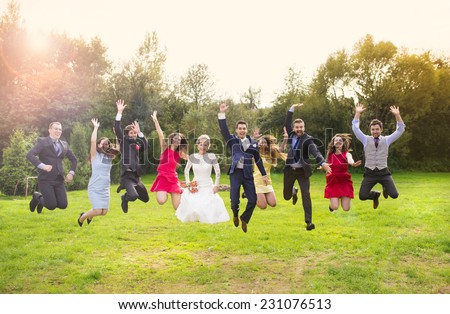 Full length portrait of newlywed couple with bridesmaids and groomsmen jumping in green sunny park