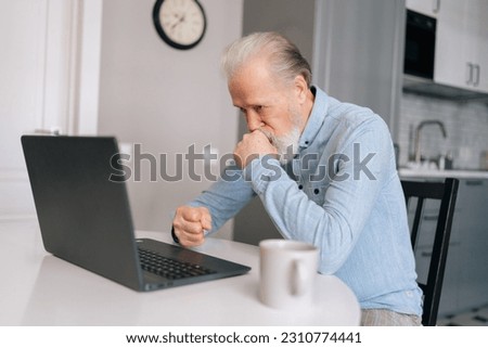 Thoughtful gray-haired mature adult man thinking about job and looking on screen of laptop computer sitting at table with coffee cup. Worried unhappy senior older man put chin on hands feels abandoned Royalty-Free Stock Photo #2310774441