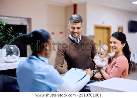 Happy parents with baby daughter registering for a doctor's appointment at pediatric reception desk. 