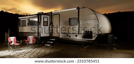 Brightly lit camping trailer at sunset with a dark ridge and bright clouds behind