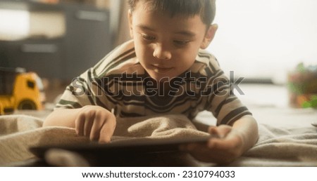 Portrait of a Focused Asian Male Kid Using Digital Tablet in his Room. Little Cute Boy Enjoying his Weekend, Playing Educational Game, Drawing Beautiful Pictures, Using Modern Technology.