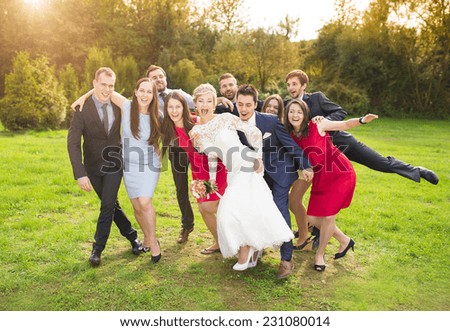 Full length portrait of newlywed couple having fun with bridesmaids and groomsmen in green sunny park