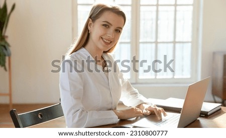 Portrait of smiling young Caucasian female nurse or doctor in white medical uniform sit at desk work on computer. Happy woman GP or physician use laptop consult patient or client online in hospital. Royalty-Free Stock Photo #2310800777