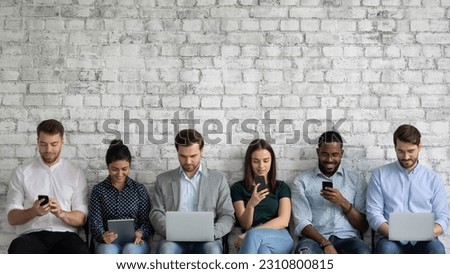Multicultural team of gadget users sitting in line, using laptops, tablets, mobile phones, working, reading messages, chatting online on social media, watching content on internet. Copy space Royalty-Free Stock Photo #2310800815