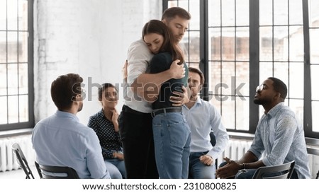 Couple of therapy group mates hugging each other on mental health meeting. Diverse team sitting in circle, welcoming teammate returning after absence, giving understanding, embrace and support Royalty-Free Stock Photo #2310800825