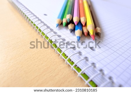 school background, colored pencils lie on a sheet of paper, an open notebook on a spiral, a college block in a cage, close-up, the concept of student writing supplies, back to school Royalty-Free Stock Photo #2310810185