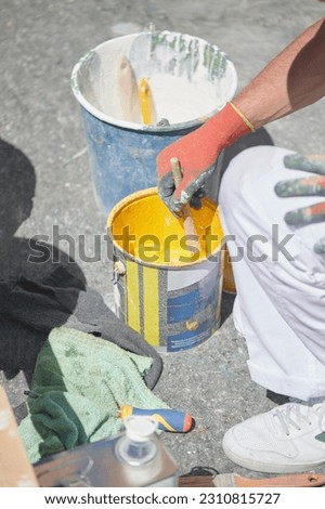 Professional painter at work. Unrecognizable young man uses a brush and a bucket to stir special acrylic paint for road marking on asphalt of a parking lot.