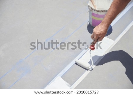 Professional painter at work. Unrecognizable young man uses a paint roller to apply special acrylic paint for road marking on asphalt.	