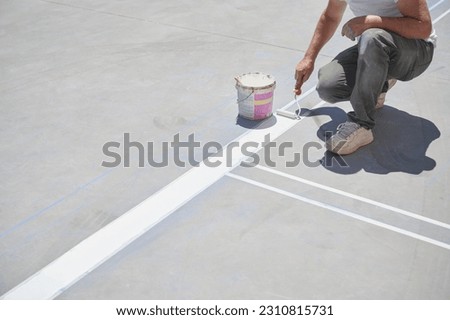 Professional painter at work. Unrecognizable young man uses a paint roller to apply special acrylic paint for road marking on asphalt.	