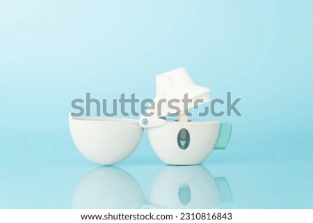 Asthma and COPD concept. Tiotropium bromide inhaler with reflection on light blue background. Pharmaceutical device of bronchodilator for lung inflammation treatment and prevent asthma attack. Royalty-Free Stock Photo #2310816843