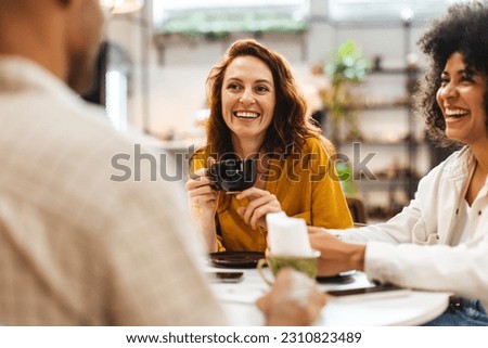 Group of young people enjoy a fun coffee date together in a cozy cafe, chatting and catching up on each other's lives. Three happy friends hanging out together on a weekend. Royalty-Free Stock Photo #2310823489