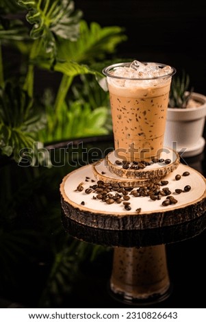 iced cappuccino coffee In a glass ready to serve Beautifully decorated with green leaves and coffee beans on a black background.
