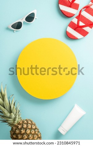 Celebrate the beauty of summer with this eye-catching top vertical view flat lay. Discover an ananas, flip-flops, spf, sunglasses on pastel blue backdrop, featuring an empty circle for text or advert