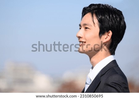 Closeup of a Japanese man in a suit on a rooftop smiling up at the sky with the city in the background Royalty-Free Stock Photo #2310850695