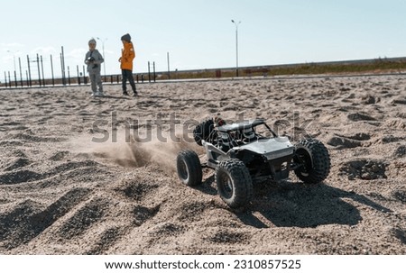 Playful baby kids driving radio controlled off road high speed sport buggy car on sand black SUV rc Royalty-Free Stock Photo #2310857525