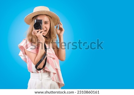 Happy young asian woman tourist smiling in summer hat standing and holding camera taking photo isolated on blue studio background with copy space for text.