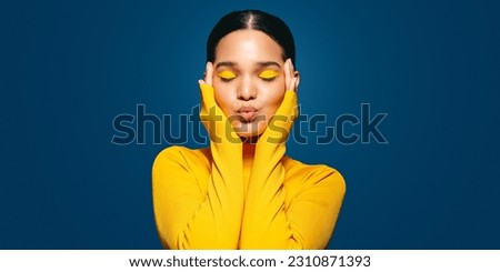 Woman embracing her face with makeup on, she is wearing colourful eyeshadow and has a confident, proud expression on her face. This young woman is taking control of her beauty and feeling self-love. Royalty-Free Stock Photo #2310871393