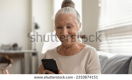 Elderly generation and modern tech. Smiling senior female use mobile phone app look at screen enjoy playing game. Happy aged woman retiree holding cell gadget chatting texting online watching video